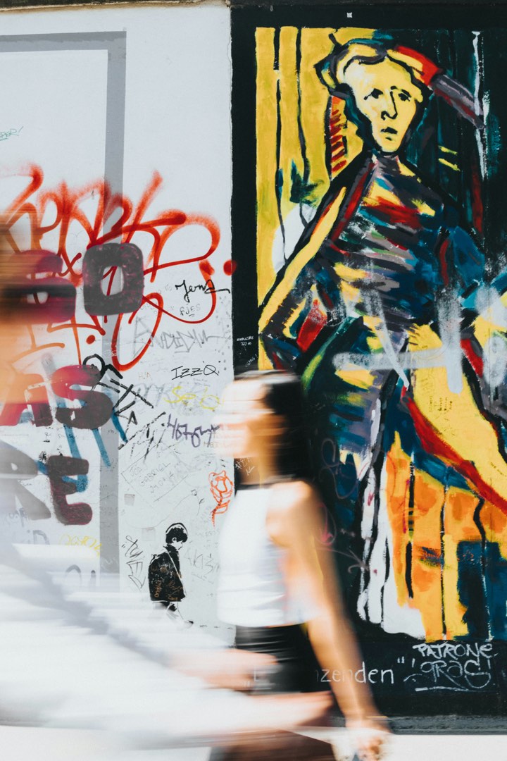 A person walks past a large, colourful painted figure on a city wall, blurred in motion.